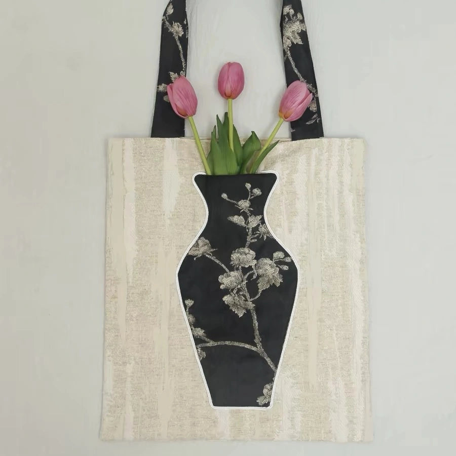 Close-up of the embroidered vase pocket on the black tote bag holding a bright red rose.