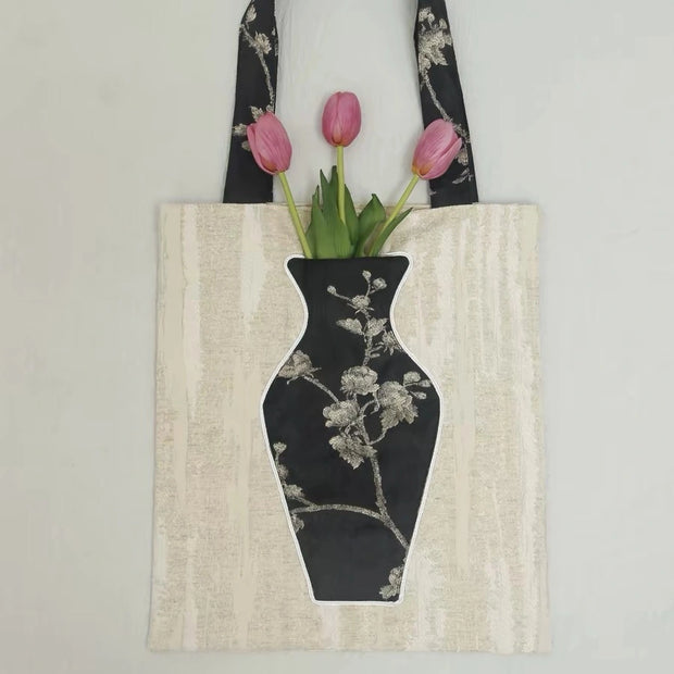 Close-up of the embroidered vase pocket on the black tote bag holding a bright red rose.