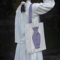 A woman in a modern white linen blazer carrying The purple Blossom Tote with a fresh red rose inserted into the embroidered vase pocket.