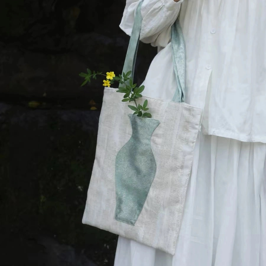 A woman in a white blazer carrying The Green Blossom Tote, an aesthetic canvas bag with an interactive vase pocket holding fresh flowers.